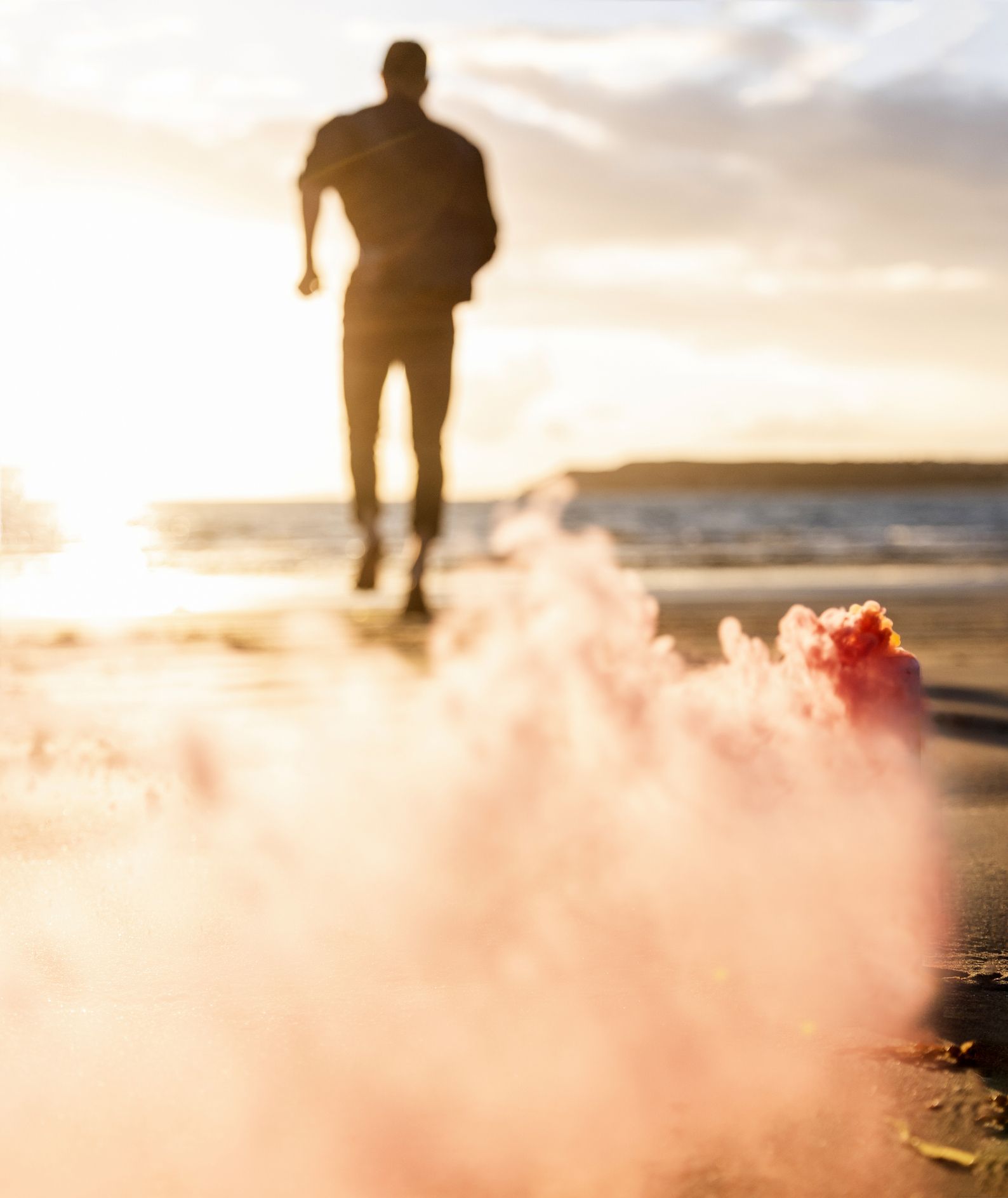 Young man running on the beach at sunset with colorful smoke